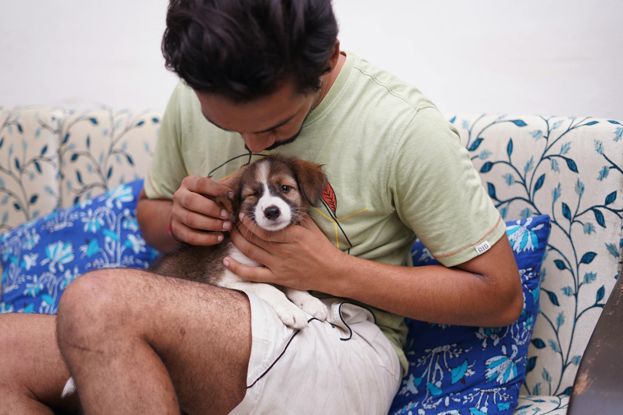 A young man affectionately cuddles a cute puppy while sitting on a floral couch.