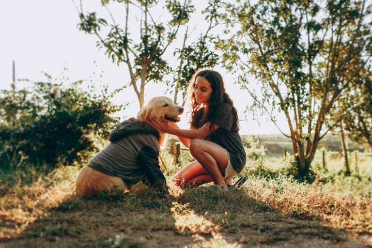 Besitzerin hockt in sonniger Natur und streichelt ihren Golden Retriever