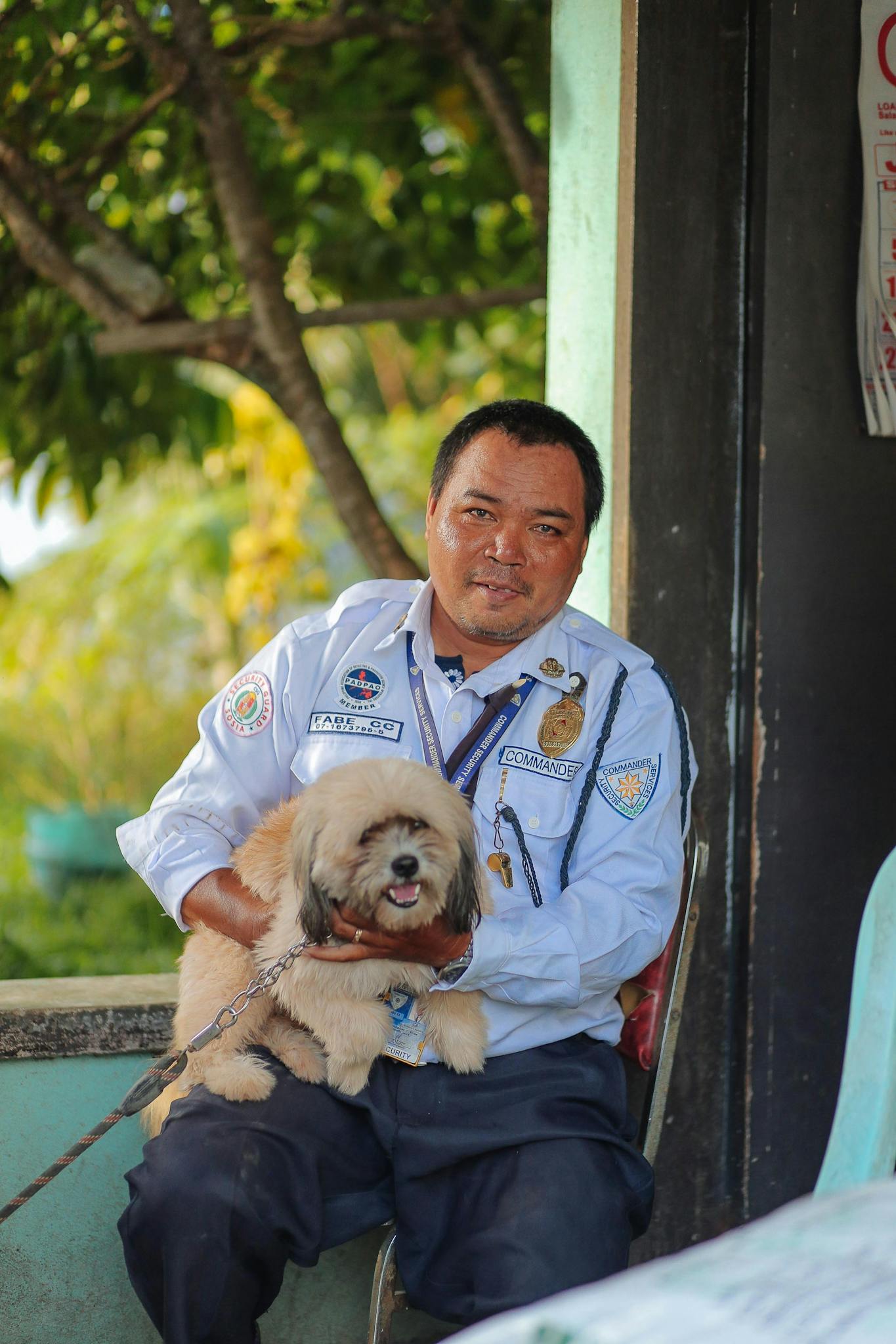 Security guard sitting with his Havanese dog outdoors during the day.